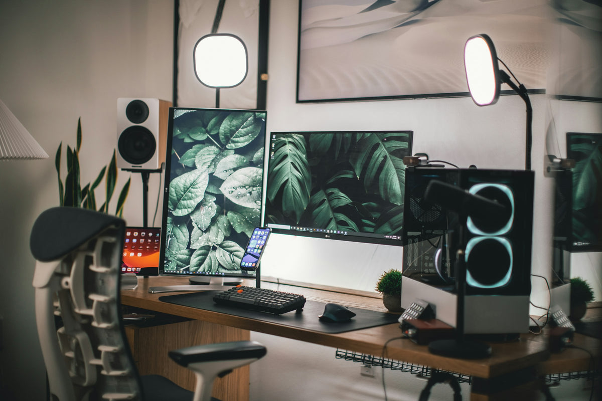 A modern desk setup with dual monitors on stands, a monitor light bar, a large desk mat and a mechanical keyboard